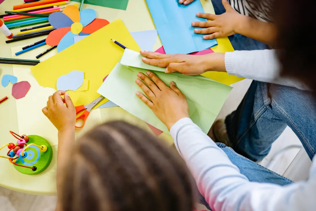 Children arranging and cutting colorful paper at a shared art table