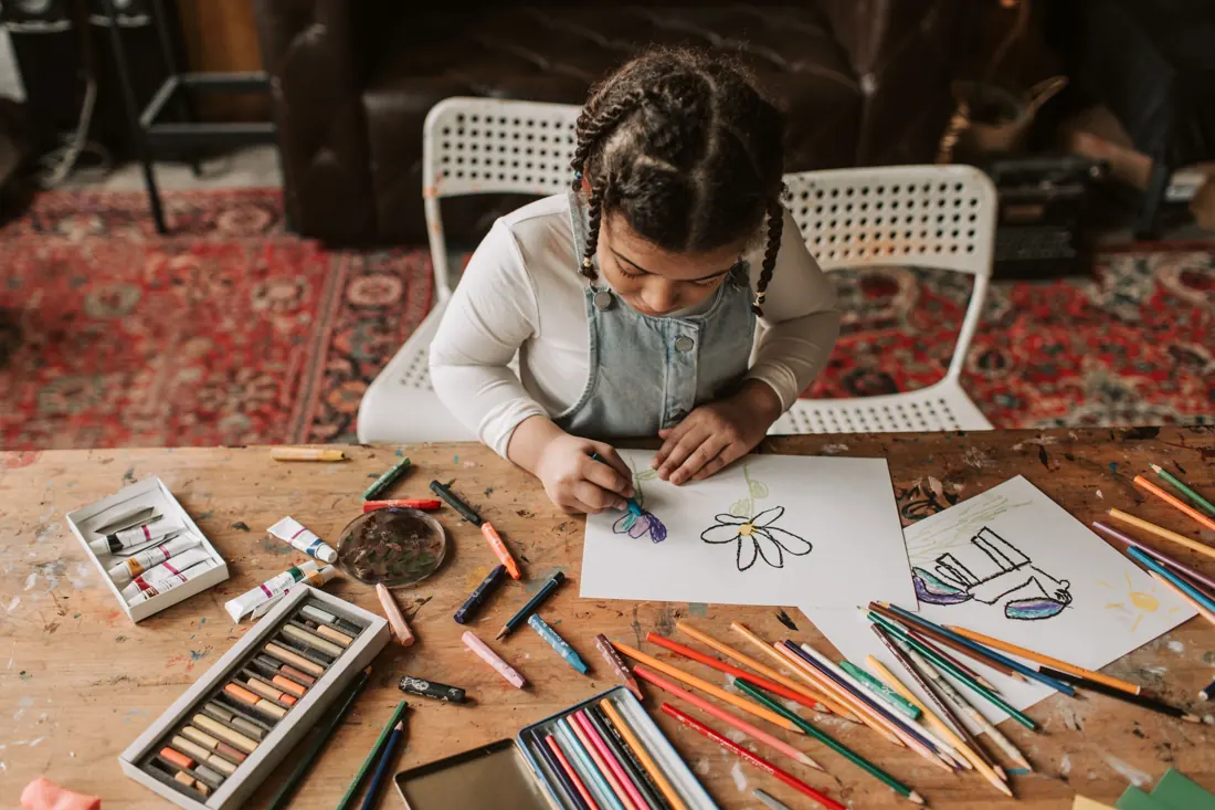 A child drawing flowers at a table with pencils and art materials